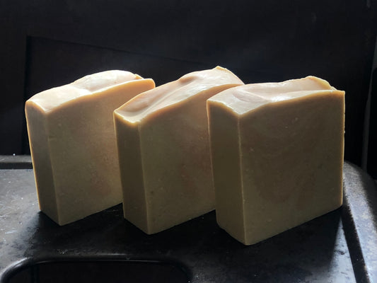 three square bars of handmade soap. cream and orange color positioned on a metal stool
