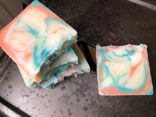 four rustic bars of soap. three are stacked. tops are bumps. soaps are cream with orange and teal swirls and sitting on rustic metal stool