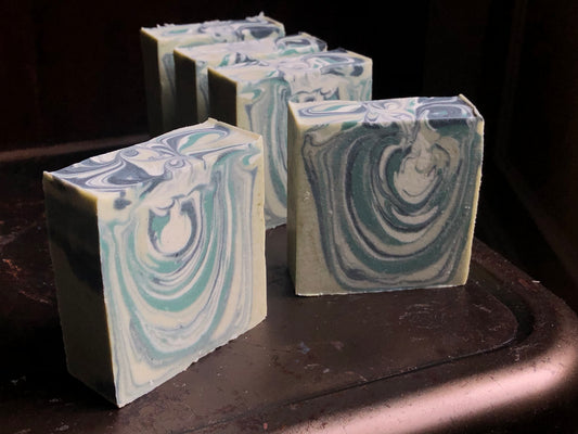 handmade soaps with swoopy layers of green, white and black sitting on a metal stool
