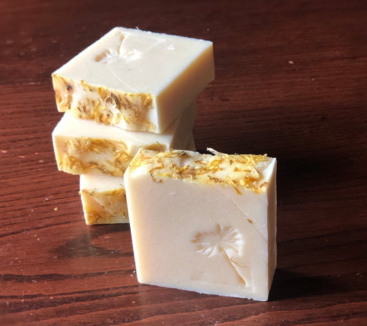 four square bars of off-white soap with flower petals on top stamped with dandelion image