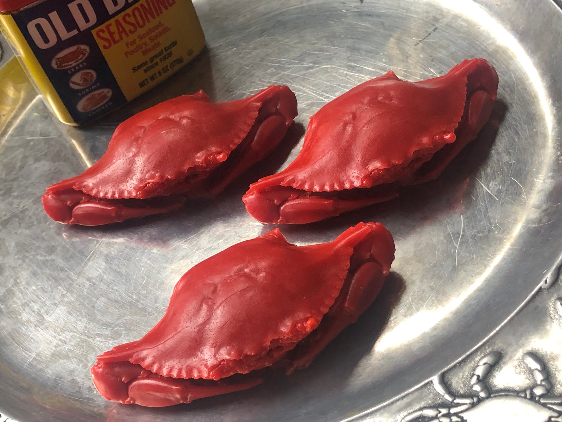 three red crab-shaped soaps on a silver tray with a can of old bay seasoning in the background