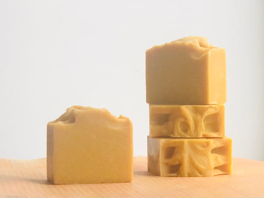 Four bars of turmeric colored soap sitting on an orange paper. Three are stacked. One stands alone. Background is whiter. 