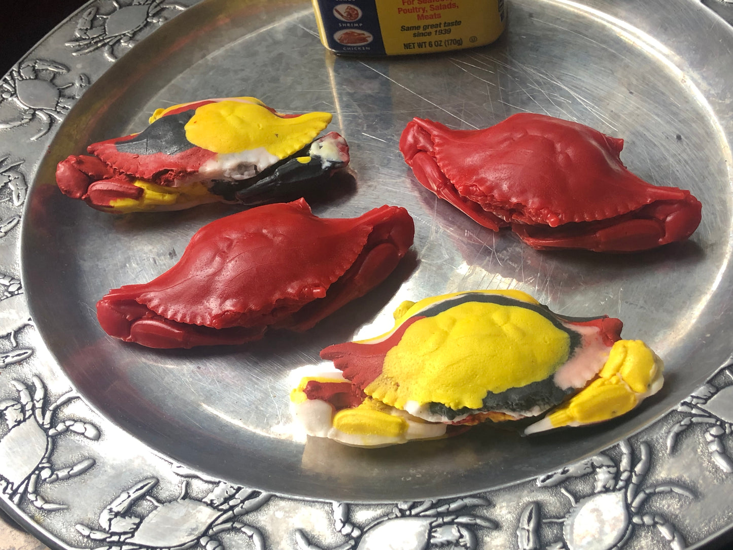 two red crab-shaped soaps and two multicolored soaps in red, black, white and yellow on a silver tray with a can of old bay seasoning in the background